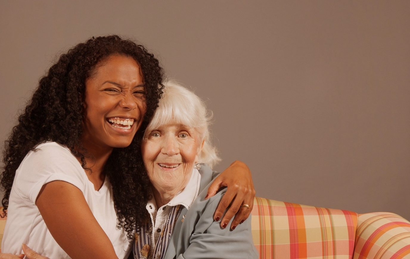 Photo of a young woman with a big smile hugging an elder.