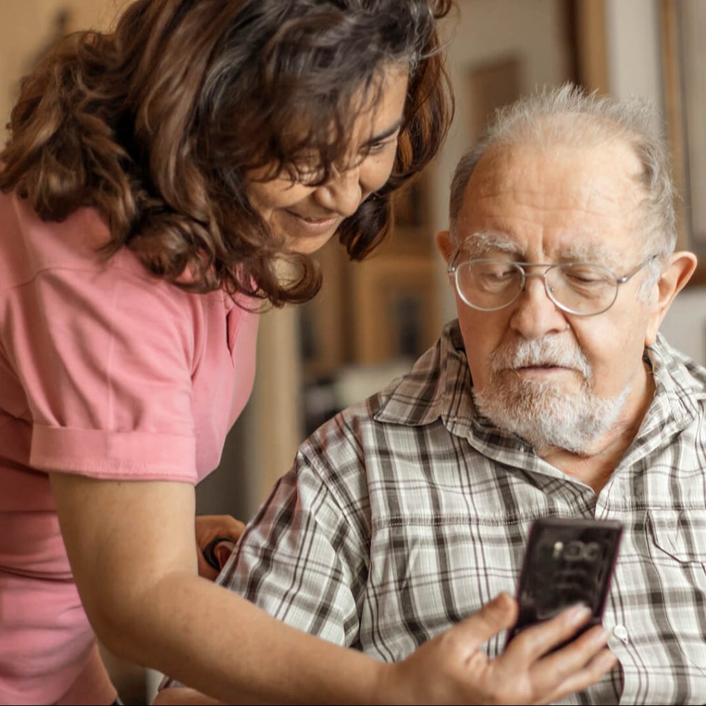 Photo of a young woman showing something on her cell phone to an elderly man.