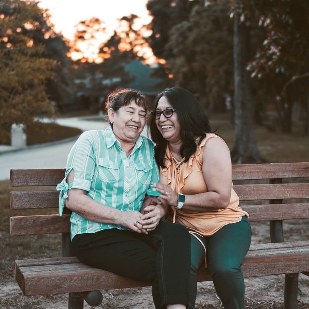 Photo of a laughing senior and her friend sitting on a park bench.