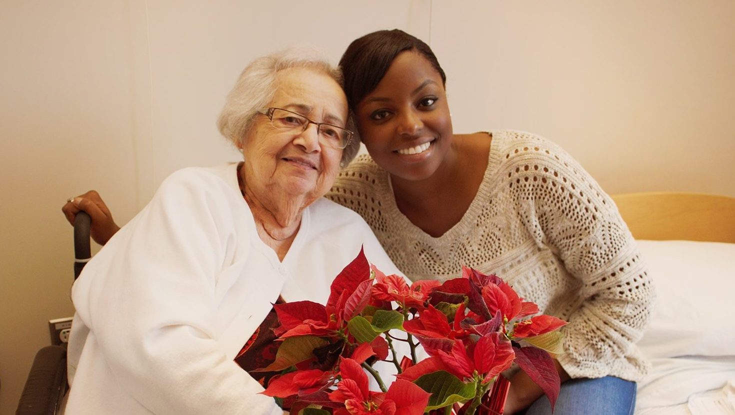 An elder and a volunteer smiling for the camera while holding a poinsettia.