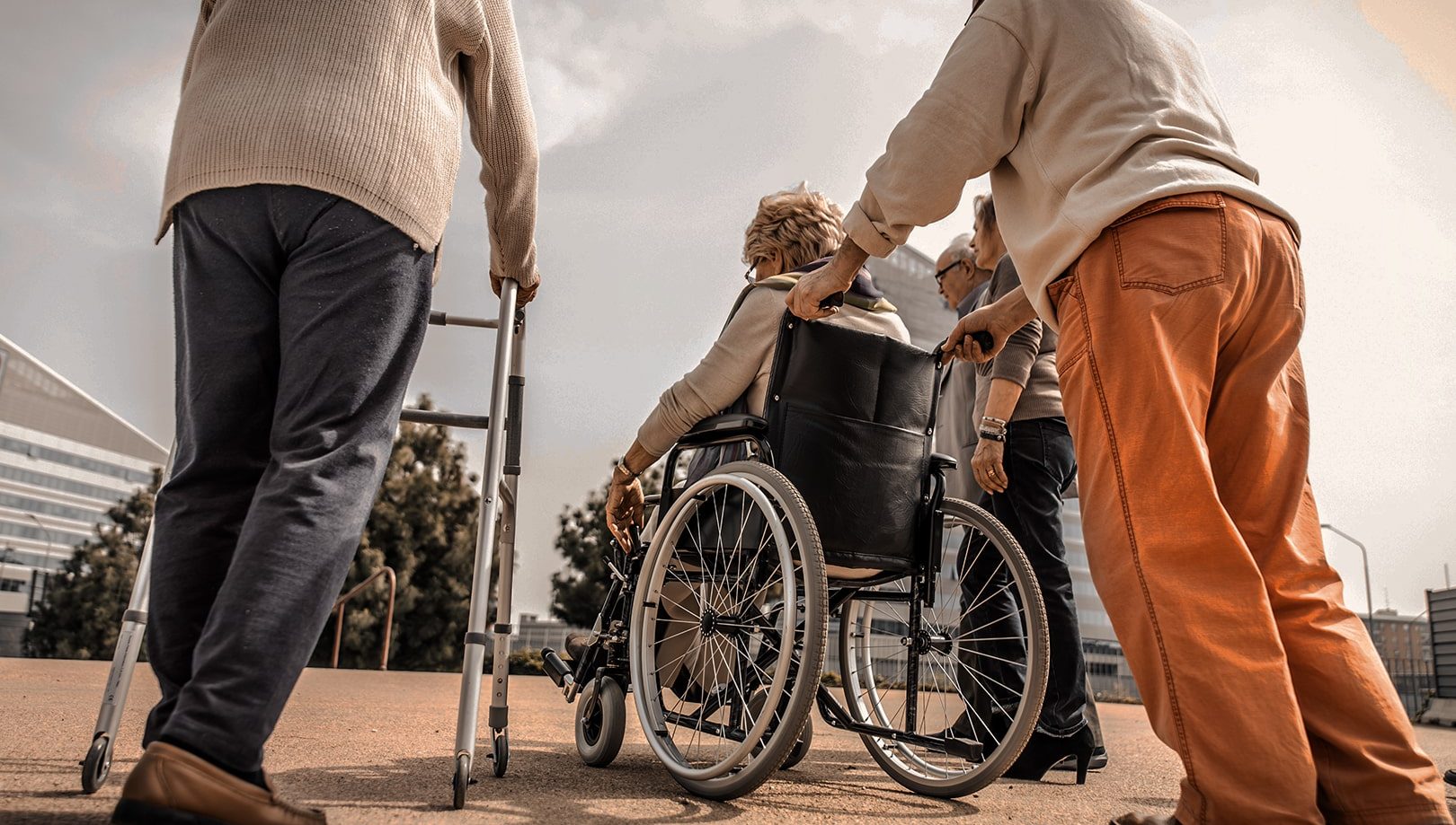 Photo de plusieurs aîné aidés dans leur déplacement. Un est en marchette, une autre en pousée en chaise roulante et une accompagnatrice support le dernier par le bras.