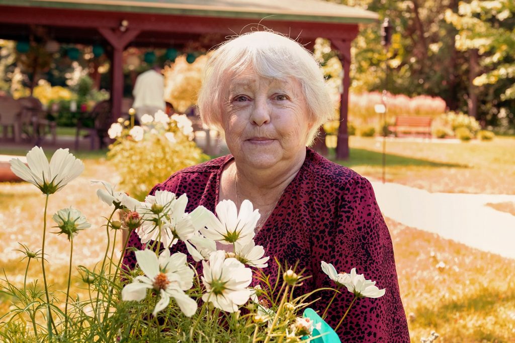 Photo d'une aînée dans un magnifique jardin ensoleillé. Il y a de jolies fleurs blanches en avant-plan.