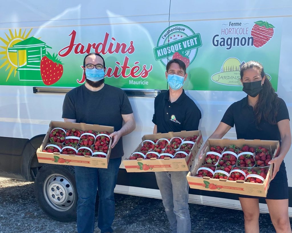 Photo of three people each holding several boxes of strawberries. They pose in front of a Gagnon horticultural farm delivery truck.