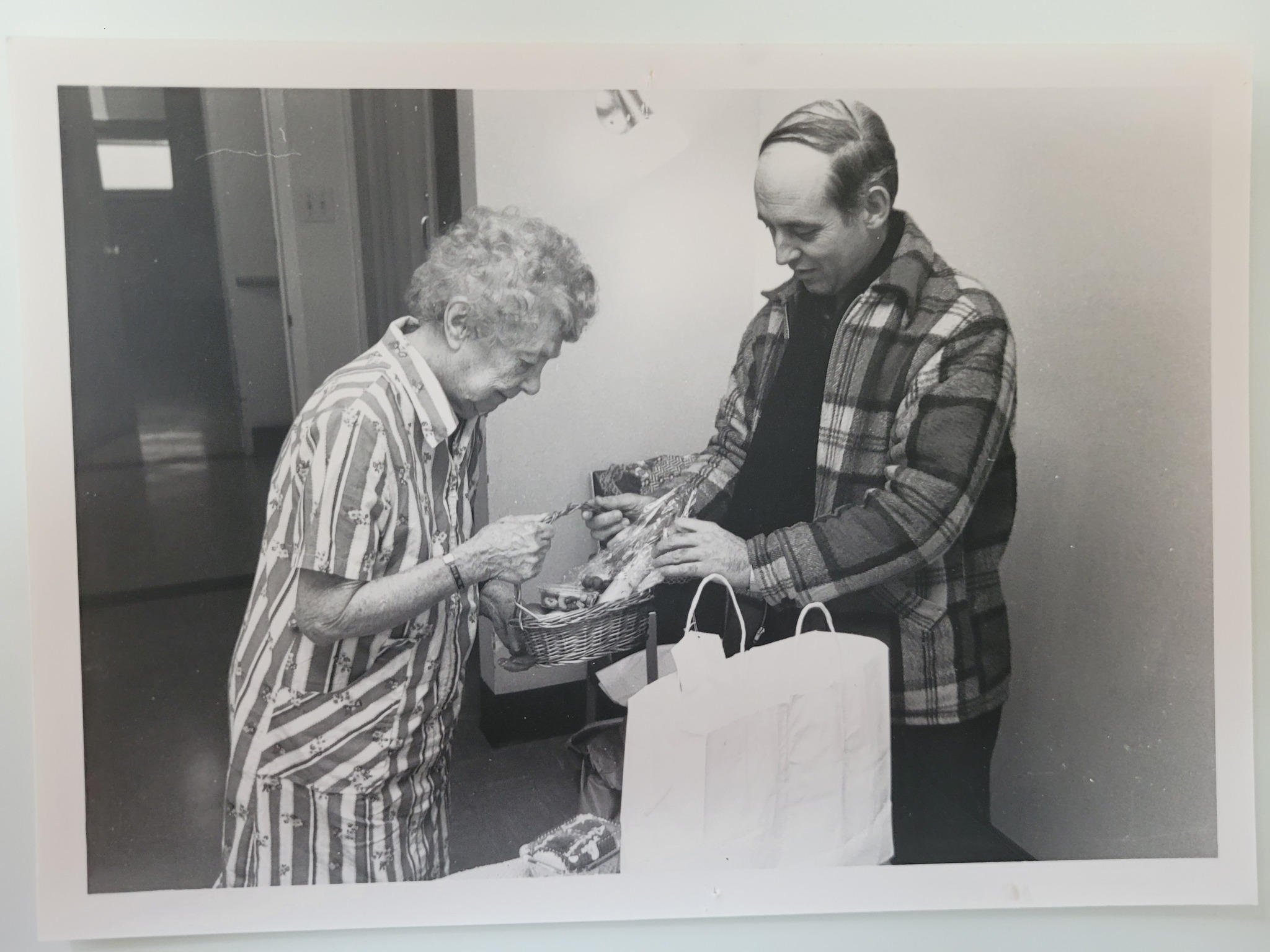 Photo d'une photo en noir et blanc de Real Longpré qui amène un panier de nourriture à une aînée.