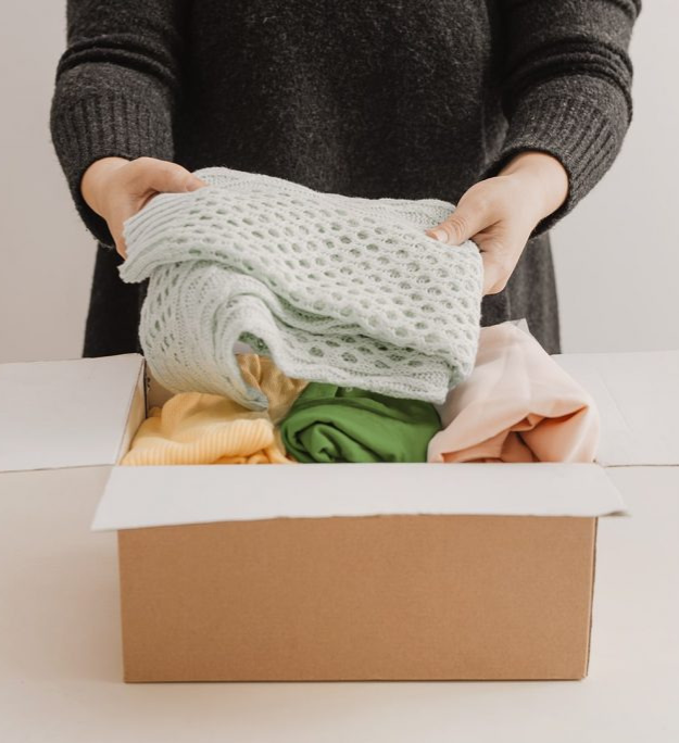Photo of a woman filling a box with neatly folded clothes.