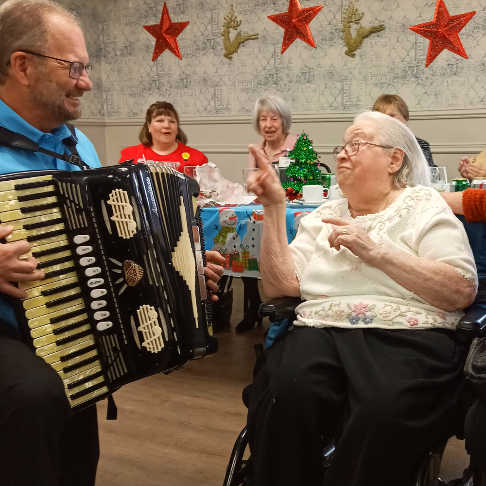 Photo of an accordion player playing a solo for a senior woman.
