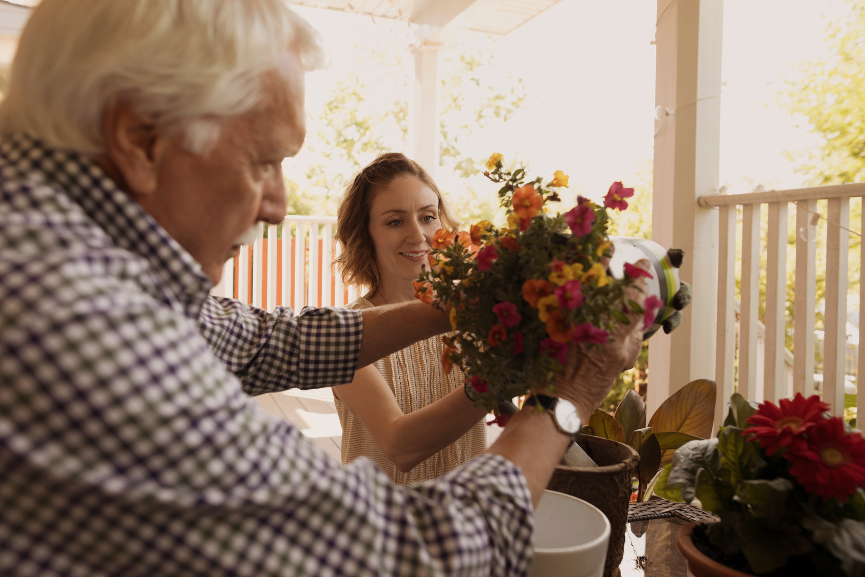 An elderly man and a young woman putting a flower bouquet into a vase.