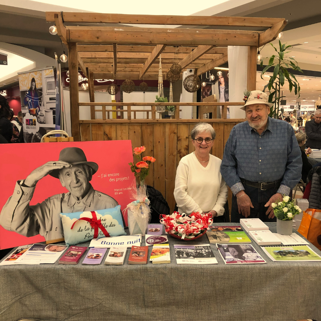 Deux personnes souriantes derrière une table avec des dépliants