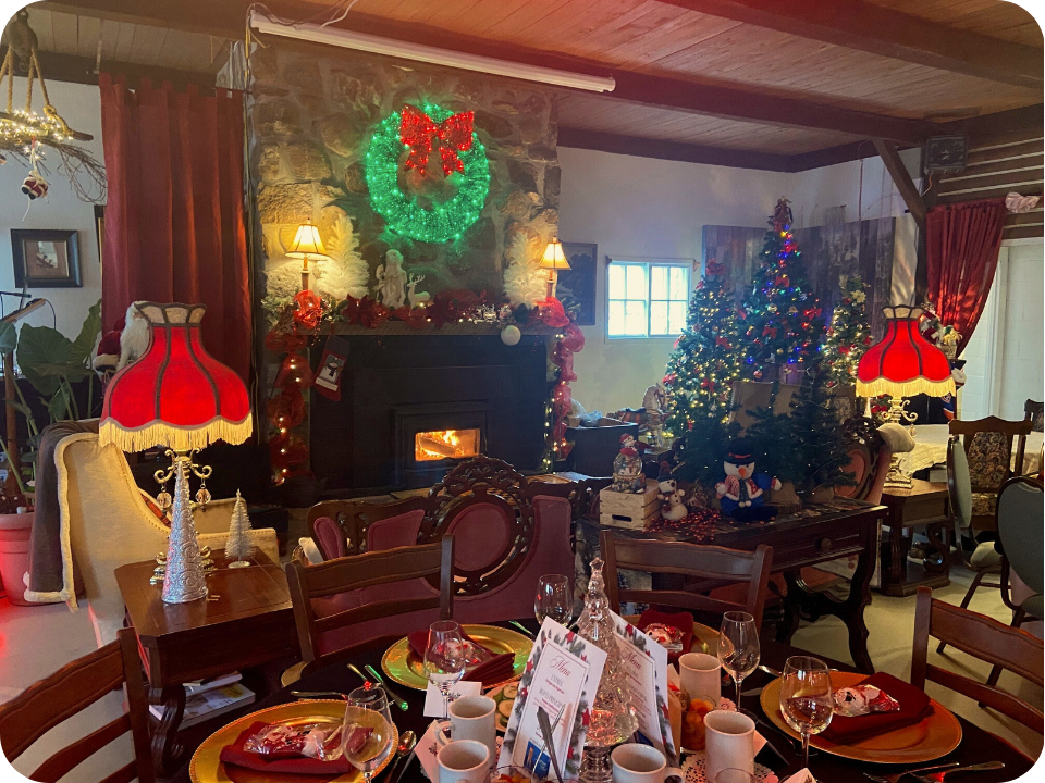 Salle décorée pour les Fêtes avec des sapins, un foyer et des tables bien mises.